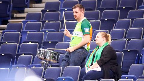 2 Fans alleine in den Reihen eines Stadions. Einer spielt eine kleine Trommel.