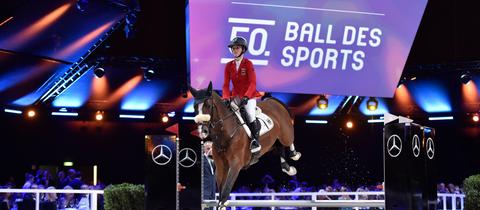 Foto vom Ball des Sports in Wiesbaden 2020. Im Hintergrund eine Werbefläche mit dem Schriftzug dazu. Im Vordergrund eine Springreiterin einem Pferd..