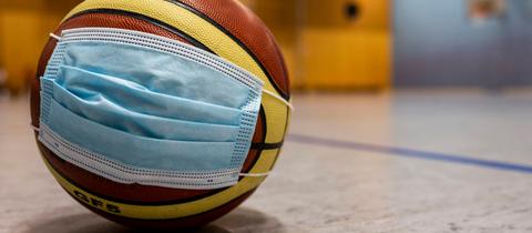 Basketball mit OP-Mundnasenschutz, der in einer Sporthalle auf dem Boden liegt.