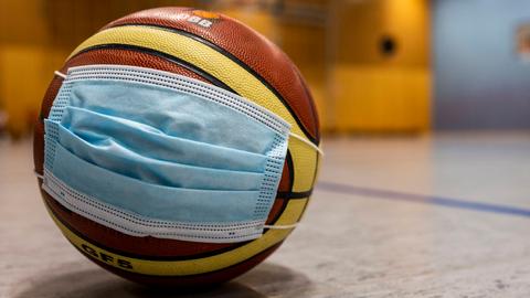 Basketball mit OP-Mundnasenschutz, der in einer Sporthalle auf dem Boden liegt.