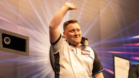 Dartsspieler Martin Schindler hebt den Arm in die Luft und grinst.