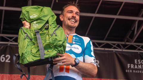 John Degenkolb hält einen Rucksack in die Höhe.