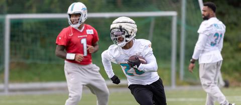 Training der Dolphins. Runningback Salvon Ahmed (M) mit einem Laufspiel neben Quarterback Tua Tagovailoa (l). 