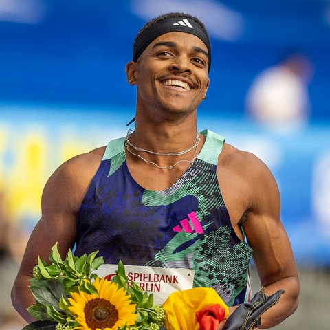 Joshua Abuaku läuft lächelnd eine Ehrenrunde. In der Hand hält er einen Blumenstrauß und eine Deutschlandfahne.