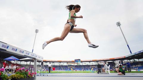 Gesa Krause in Leichtathletikwettkampfkleidung springend in der Luft - aus der Froschperspektive fotografiert.