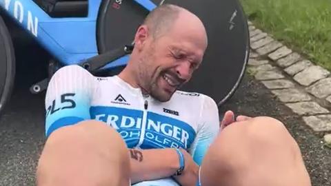 Triathlet Patrick Lange liegt mit schmerzverzerrtem Gesicht auf der Straße.