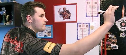 Fabian Schmutzler steht an einer Dartsscheibe und hat einen Pfeil in der Hand.
