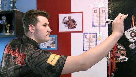 Fabian Schmutzler steht an einer Dartsscheibe und hat einen Pfeil in der Hand.