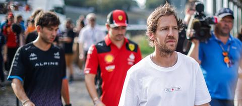 Sebastian Vettel dahinter zwei aktuelle Formel 1-Rennfahrer und ein Kameramann.