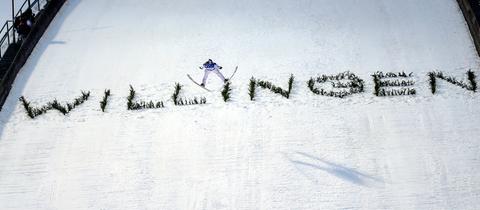 Eine Springschanze von vorne, in welche das Wort "Willigen" eingearbeitet wurde. In der Mitte, ganz klein, ein Skispringer von vorne.