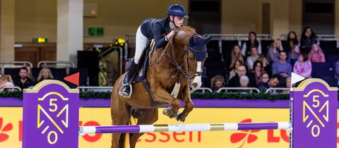 Eva Kunkel springt mit ihrem Pferd über ein lila Hinderniss.