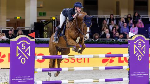 Eva Kunkel springt mit ihrem Pferd über ein lila Hinderniss.