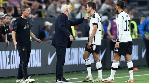 Zwei Fußballspieler in weißen Trikots sprechen mit ihrem schwarz gekleideten Trainer am Spielfeldrand.