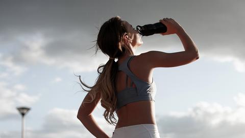 Sportlerin trinkt aus Tinkflasche und blickt Richtung Sonne