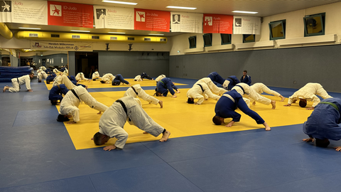 Jugendliche in Judo-Anzügen rollen auf einer Matte herum