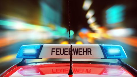 Feuerwehrauto mit Blaulicht und Schriftzug "Feuerwehr" auf einer dunklen Straße mit bunten Lichtern