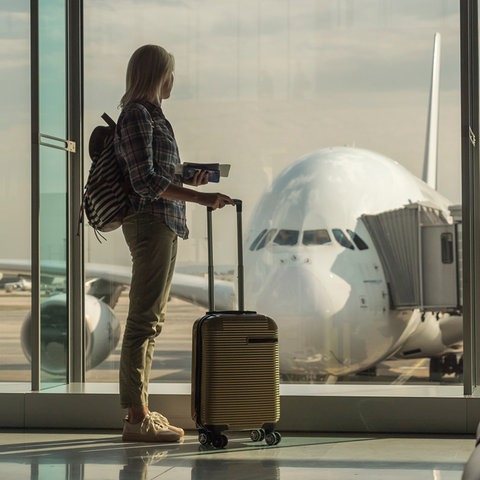 Flughafen, Frau wartet am Gate auf das Boarding mit einem Trolley in der Hand