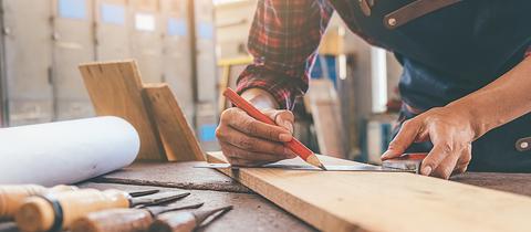 Handwerker zeichnet mit Bleistift auf Holz