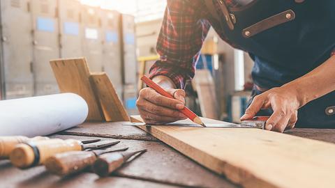 Handwerker zeichnet mit Bleistift auf Holz