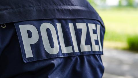 Rücken eines Polizisten mit Schriftzug "Polizei" auf einer blauen Jacke