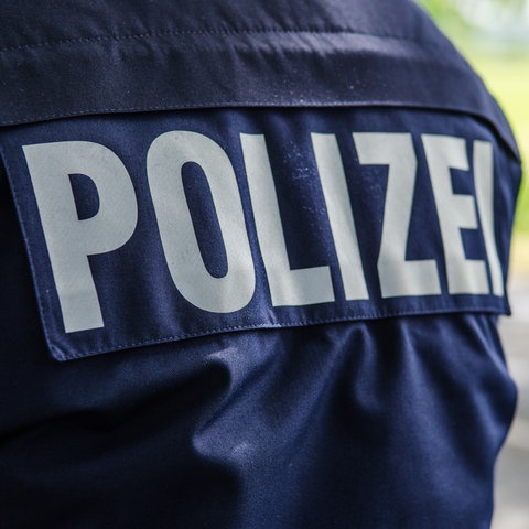 Rücken eines Polizisten mit Schriftzug "Polizei" auf einer blauen Jacke