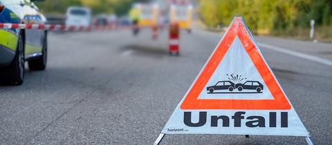 Gesperrte Autobahn mit Symbol-Schild "Unfall" im Vordergrund, Absperrband und Polizeiauto
