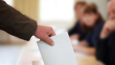 Hand mit einem gefalteten Wahlzettel, wirft den Wahlzetteel in eine Box