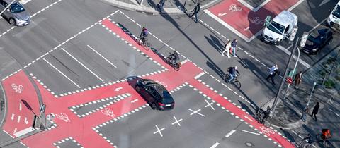 Radfahrer, Fußgänger und Autos sind an einer Kreuzung nahe der Alten Oper, die mit roten Fahrradspuren markiert ist, unterwegs.
