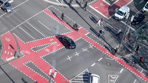 Radfahrer, Fußgänger und Autos sind an einer Kreuzung nahe der Alten Oper, die mit roten Fahrradspuren markiert ist, unterwegs.