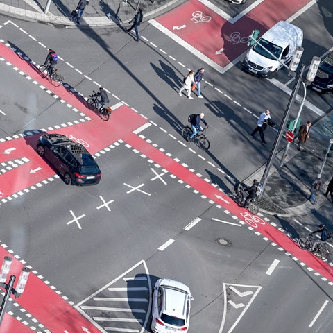 Radfahrer, Fußgänger und Autos sind an einer Kreuzung nahe der Alten Oper, die mit roten Fahrradspuren markiert ist, unterwegs.