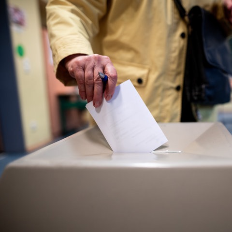 Eine Frau wirft einen Wahlschein in eine Wahlurne.