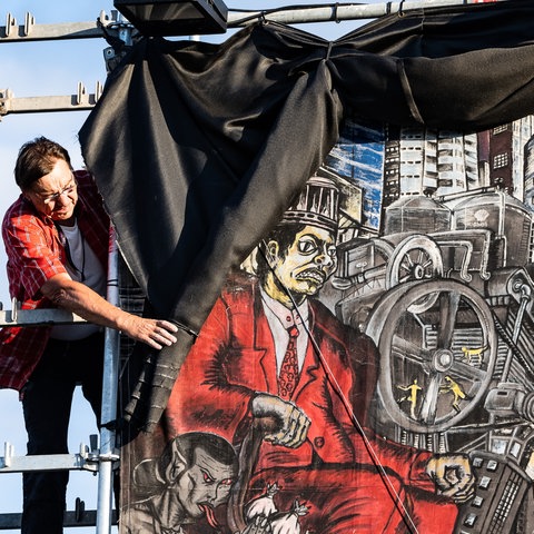 A worker stands at the top of a scaffold and rolls black fabric over a large-format, very small-scale colored image.