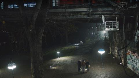 3 Menschen nachts im spärlich beleuchteten Park unter einer Stahlbrücke
