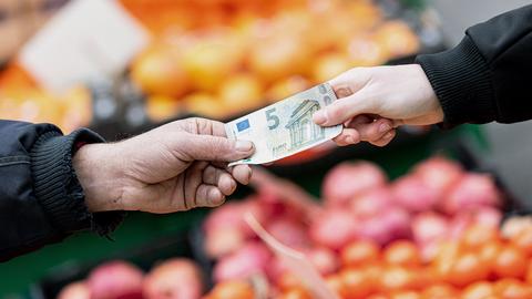 5 Euro Schein wechselt den Besitzer, im Hintergrund Gemüse, Obst etc.