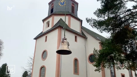 EIne Glocke wird an einem Seil zum Kirchturm hochgezogen.