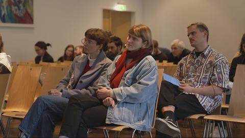 Menschen sitzen in Saal und hören einem Redner zu