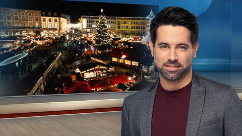 hessenschau-Moderator Daniel Johé im Fernsehstudio. Im Hintergrund ein Bild von einem Weihnachtsmarkt.