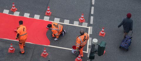 Arbeiter richten auf einer Straße einen roten Radweg-Streifen ein 