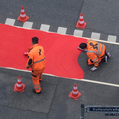 Arbeiter richten auf einer Straße einen roten Radweg-Streifen ein 