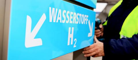 Wasserstoff H2O steht auf einem blauen Schild mit Pfeil nach links und ein Mann daneben stehend.
