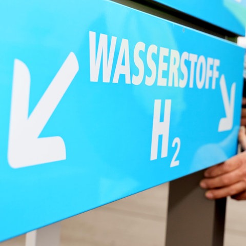 Hydrogen H2O è scritto su un cartello blu con una freccia che punta a sinistra e un uomo in piedi accanto ad essa.