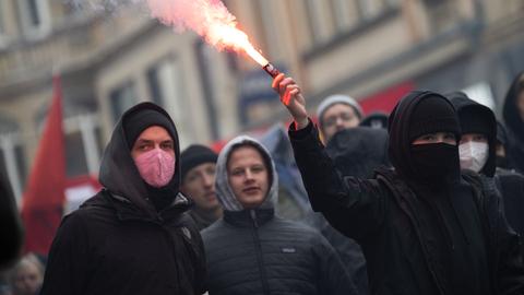 Dunkel gekleidete Menschen in einer Gruppe auf der Straße. Eine Person hält ein rauchendes Leuchtfeuer in der Hand.