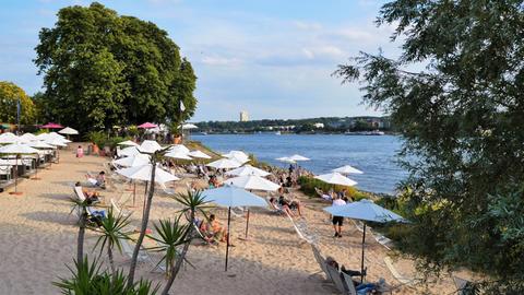 Strand am Fluss, Menschen auf Liegestühlen unter Sonnenschirmen