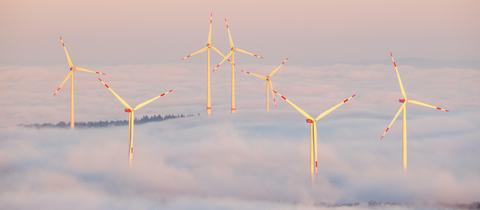 Blick auf Windräder, die aus "rosa" Nebel herausragen.