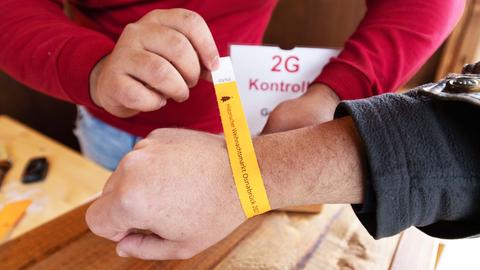 Zwei Hände legen einer dritten Hand ein orangfarbenes Papierbändchen um das Handgelenk mit der Aufschrift "Weihnachtsmarkt Osnabrück".