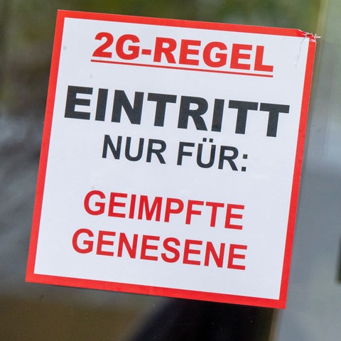 Ein Schild mit der Aufschrift "2G Regel - Eintritt nur für: Geimpfte oder Genesene" steht  vor einer Bar.