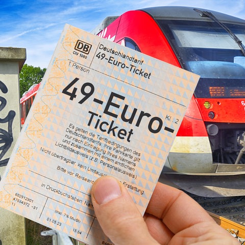 49-Euro-Ticket in der Hand, dahinter Regionalbahn