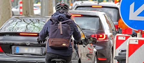 Eine Radfahrerin wird auf einer durch Baumaßnahmen verengten Straße von Autos überholt.