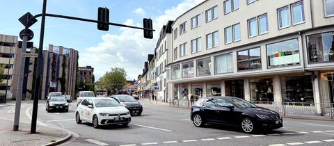 Straße mit vier Autospuren, darauf mehrere Autos, die an einer Ampel anfahren.