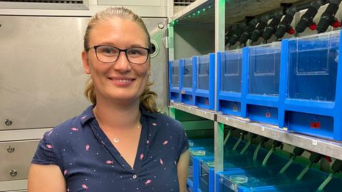 Doktorandin Annalena Barth an ihrem Forschungsort - der Garnelenfarm, sie lächelt, trägt eine blaue Kurzarmbluse mit Muster, Brille, die Haare zum Zopf zurückgekämmt.